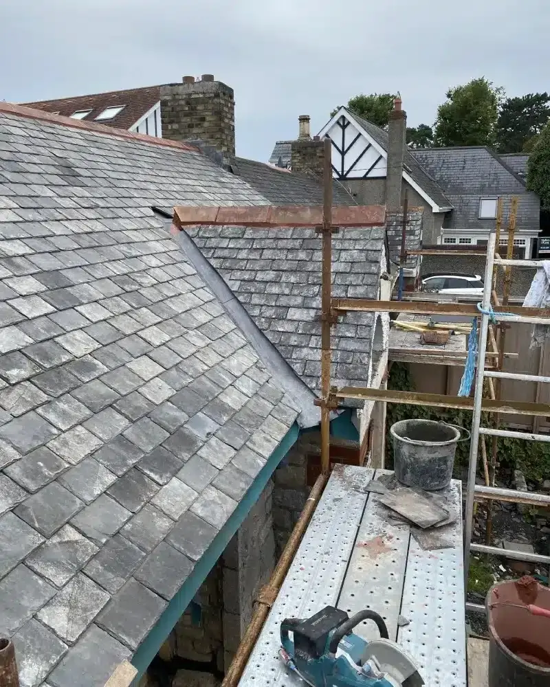 Slate roof with a red hip trim beside a scaffold platform with a saw on it