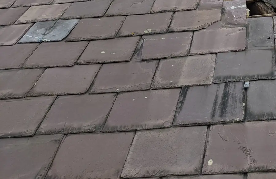 Close view of slipped and cracked slates on an old slate roof